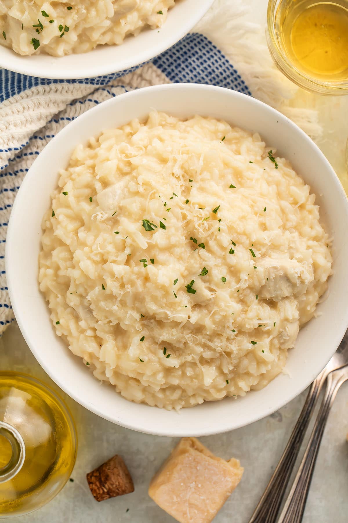 A large white bowl of Instant Pot chicken risotto on a table with a blue and white kitchen towel next to a glass of white wine.