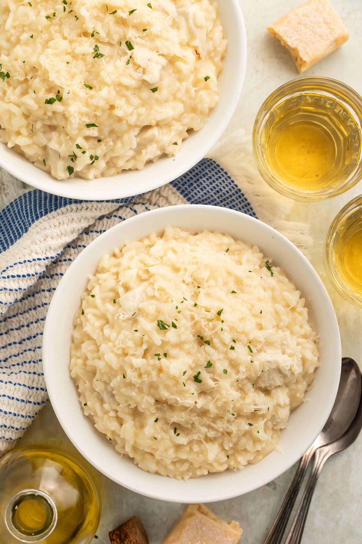 A large white bowl of Instant Pot chicken risotto on a table with a blue and white kitchen towel next to a glass of white wine.