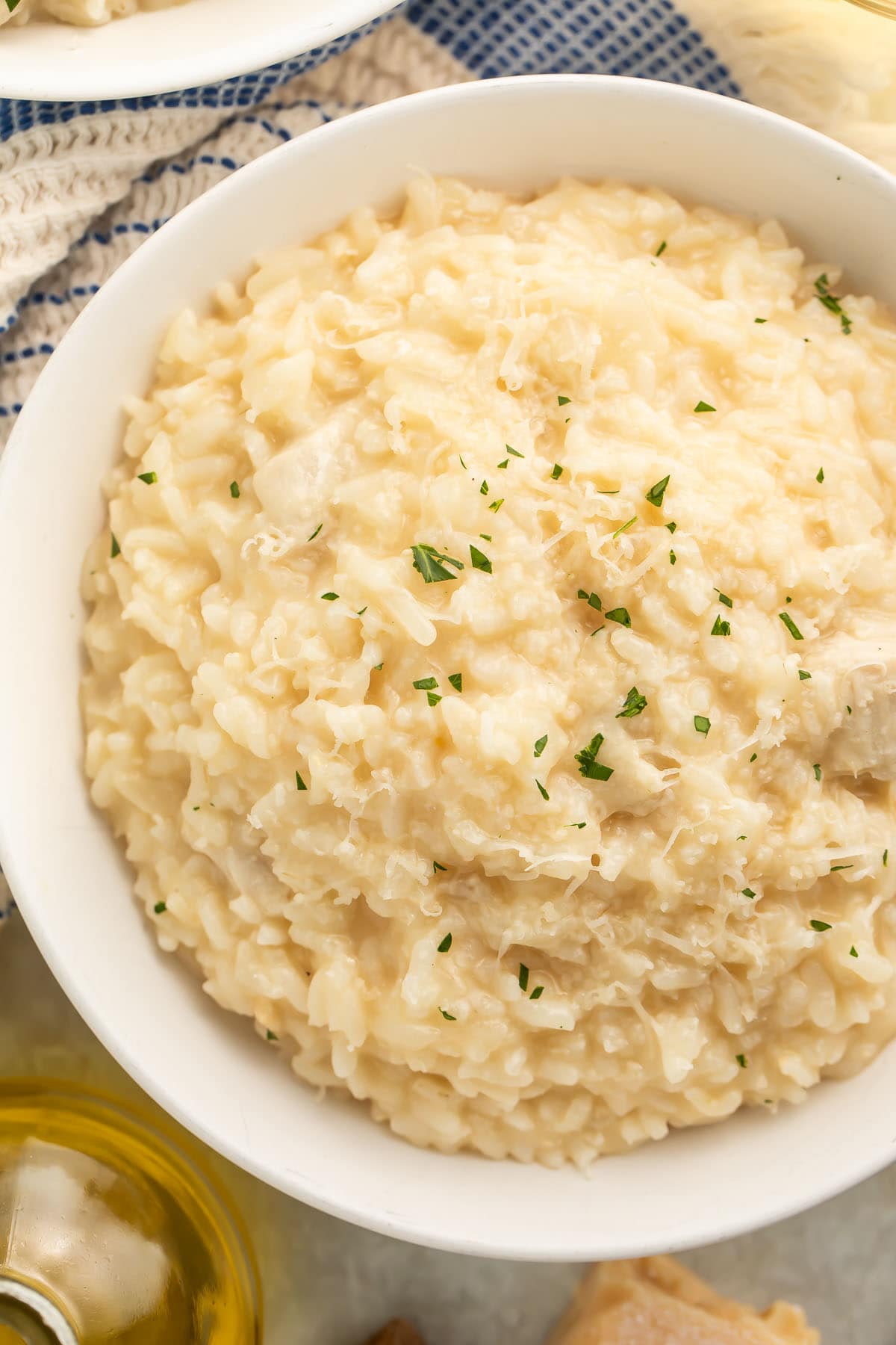 A large white bowl of Instant Pot chicken risotto on a table with a blue and white kitchen towel next to a glass of white wine.