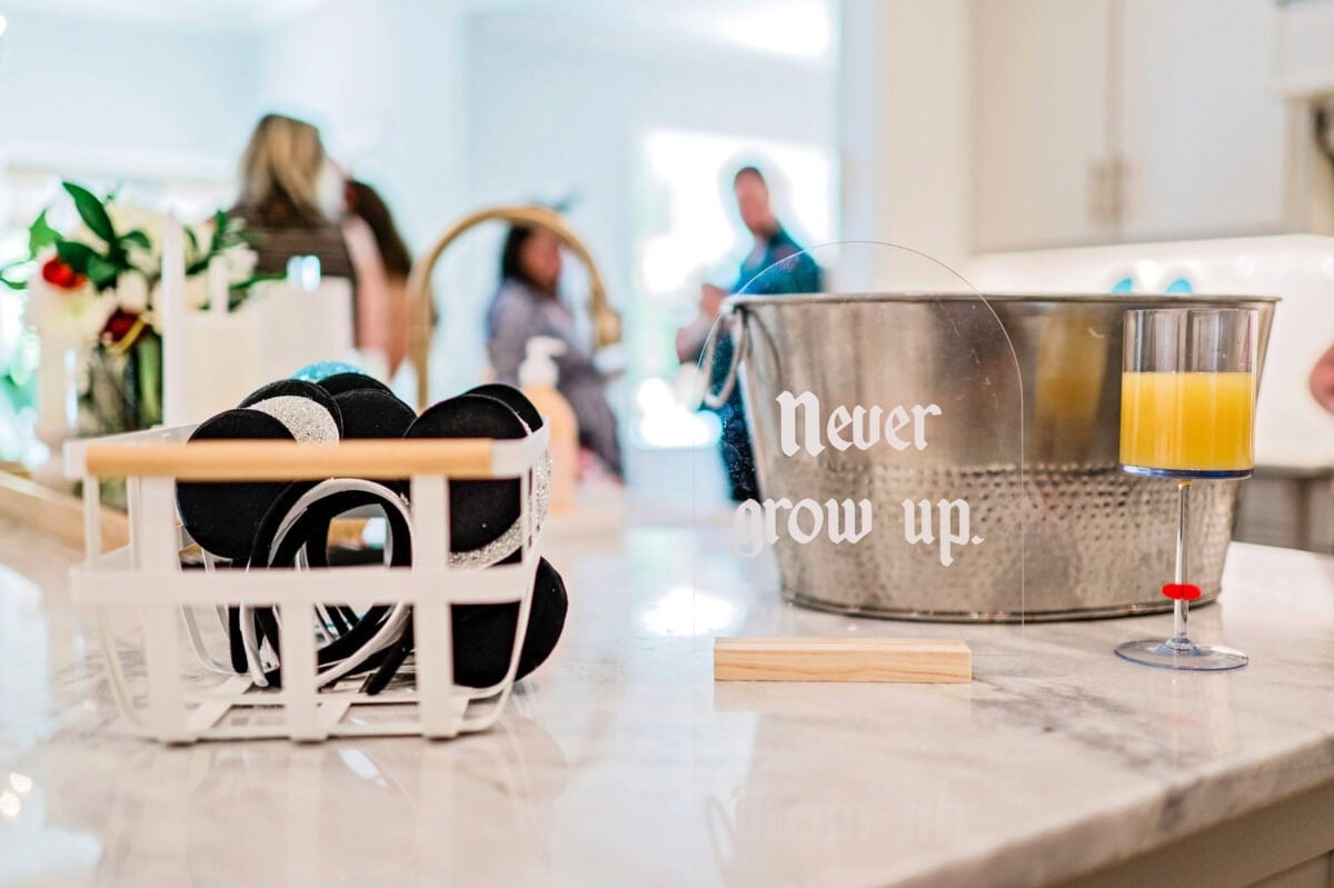 An acrylic "Never Grow Up" sign sits on a countertop next to a basket of mouse ear headbands.