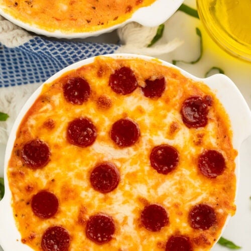Two cottage cheese pizza bowls topped with pepperoni on a table with shreds of fresh basil.