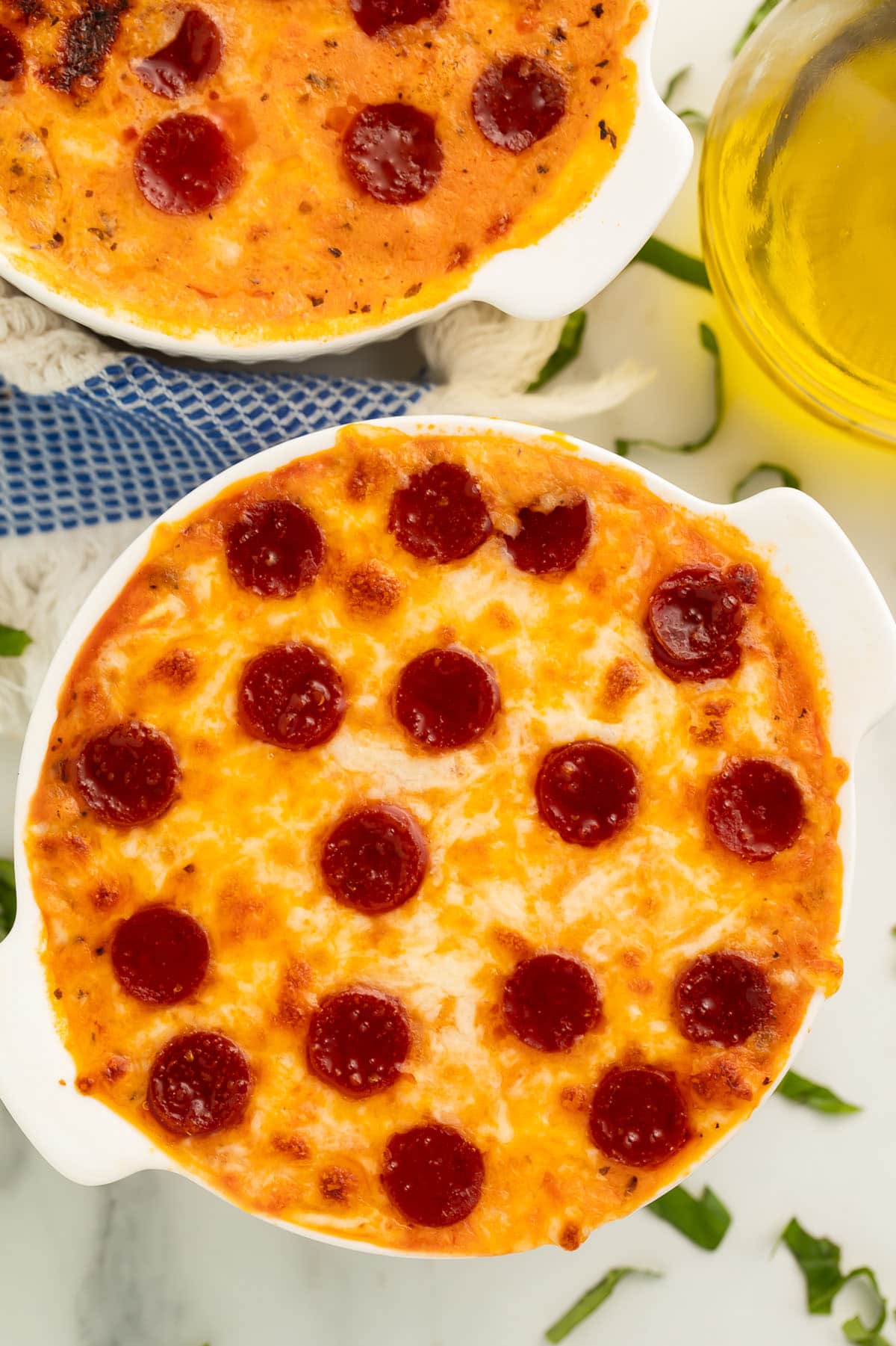 Two cottage cheese pizza bowls topped with pepperoni on a table with shreds of fresh basil.