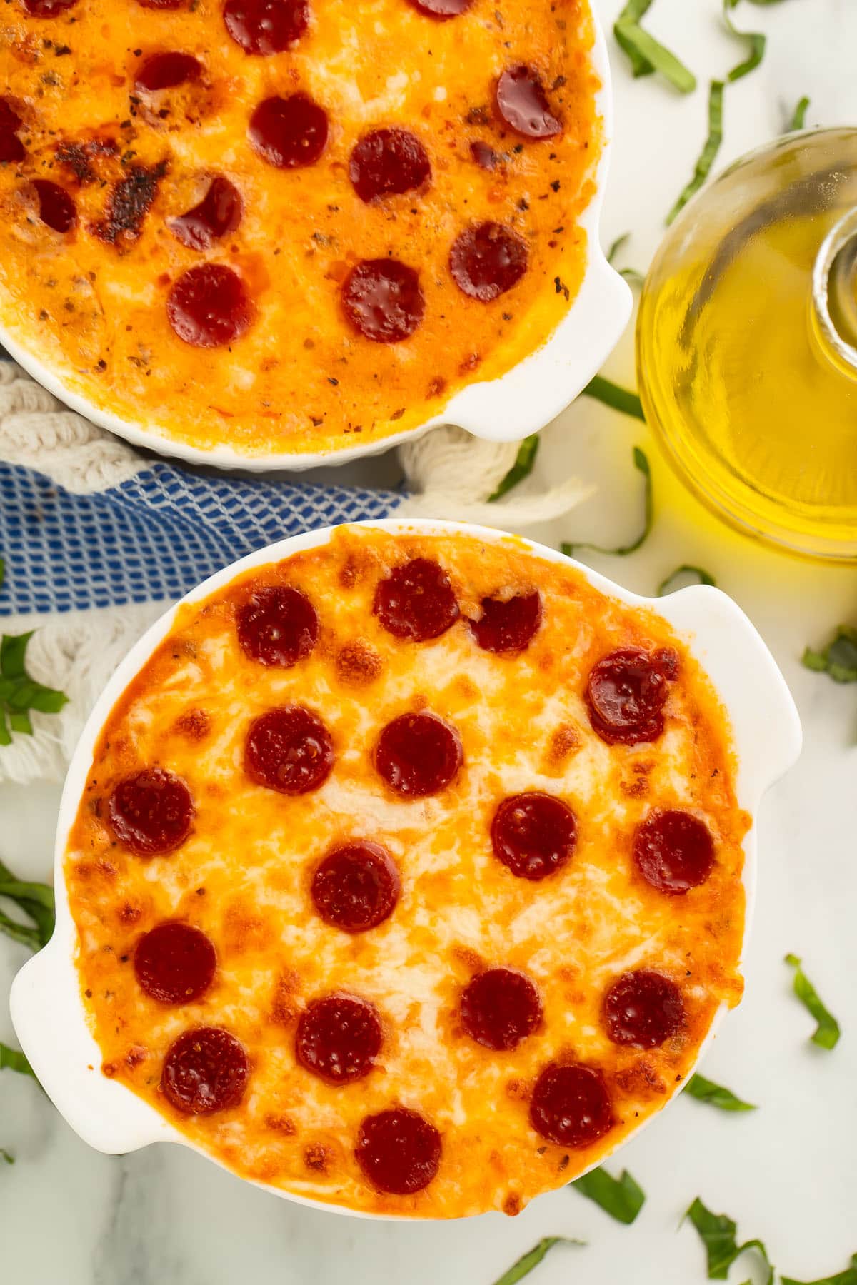 Two cottage cheese pizza bowls topped with pepperoni on a table with shreds of fresh basil.