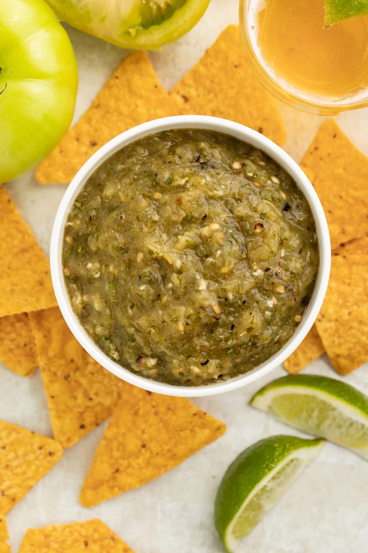 Overhead view of a bowl of chunky green tomato salsa surrounded by triangular tortilla chips.