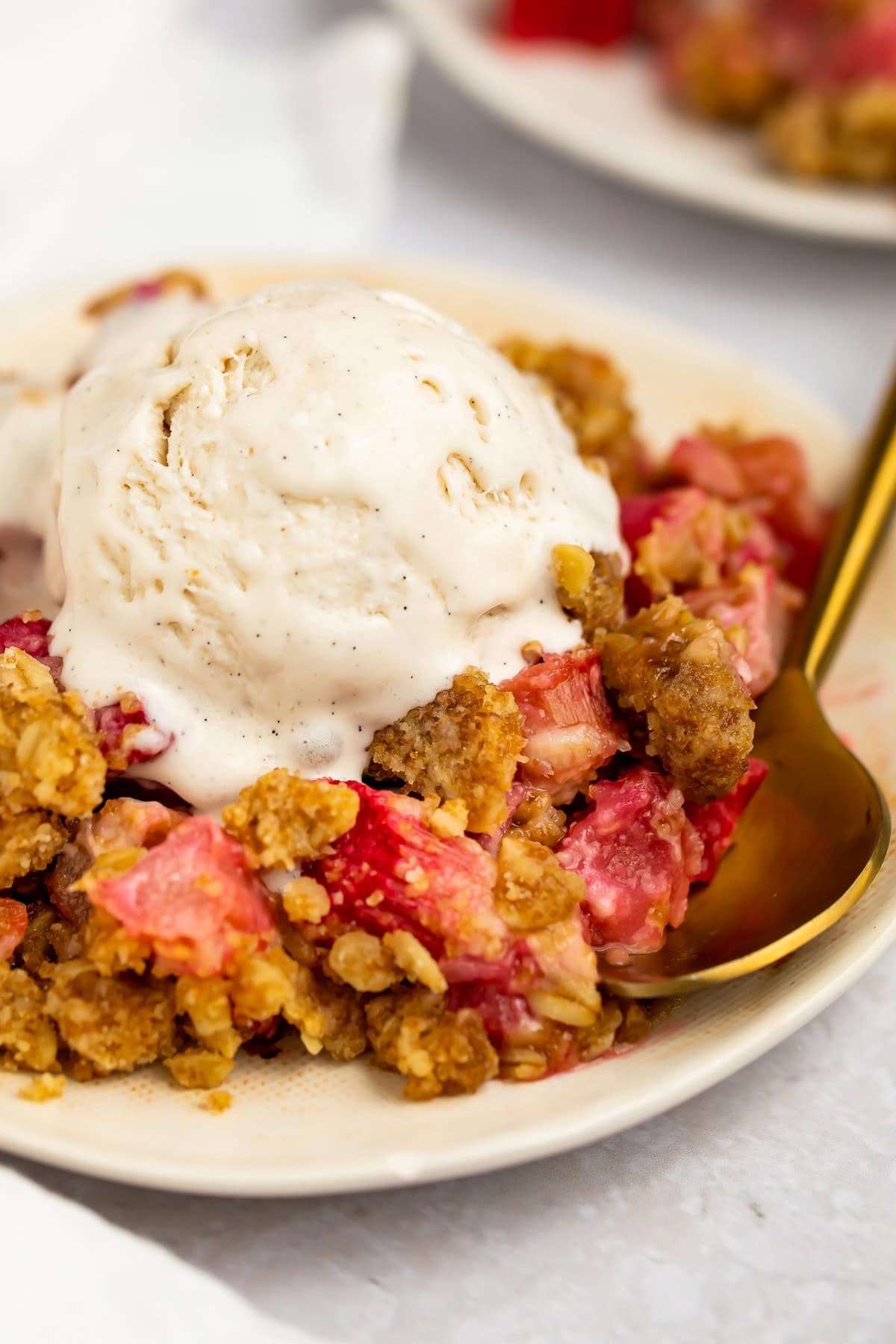 A scoop of rhubarb crumble topped with vanilla ice cream on a plate.