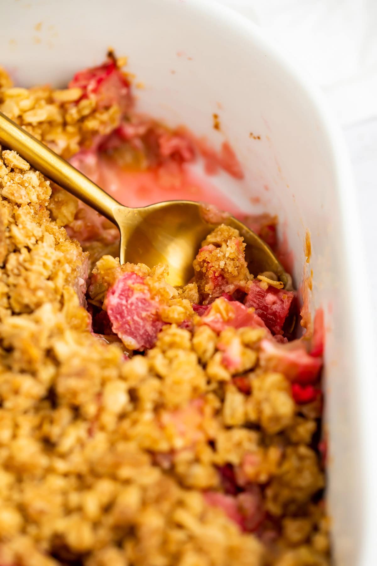 A gold spoon resting in a baking dish of rhubarb crumble.
