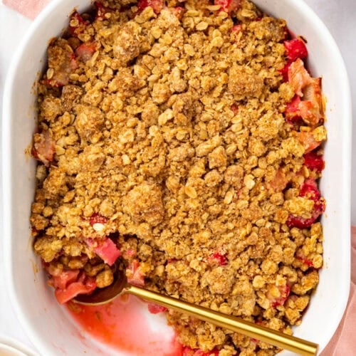 Overhead photo of a white oval baking dish holding rhubarb crumble with a gold spoon.