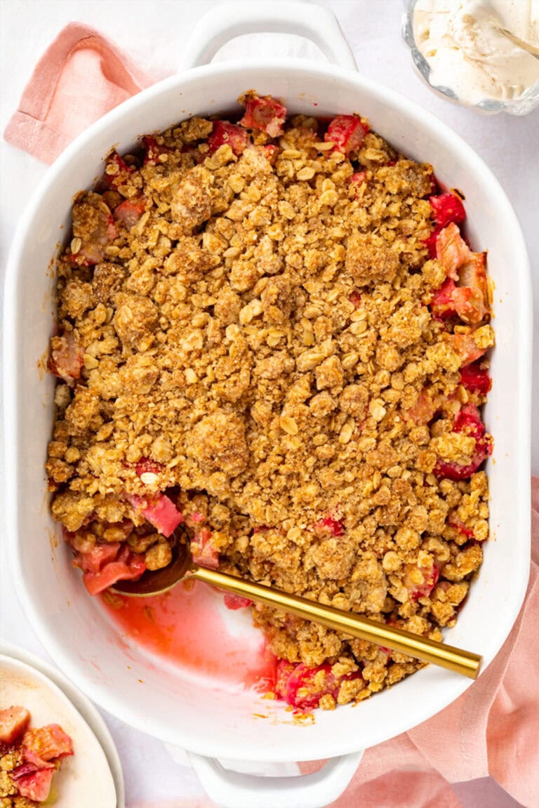 Overhead photo of a white oval baking dish holding rhubarb crumble with a gold spoon.