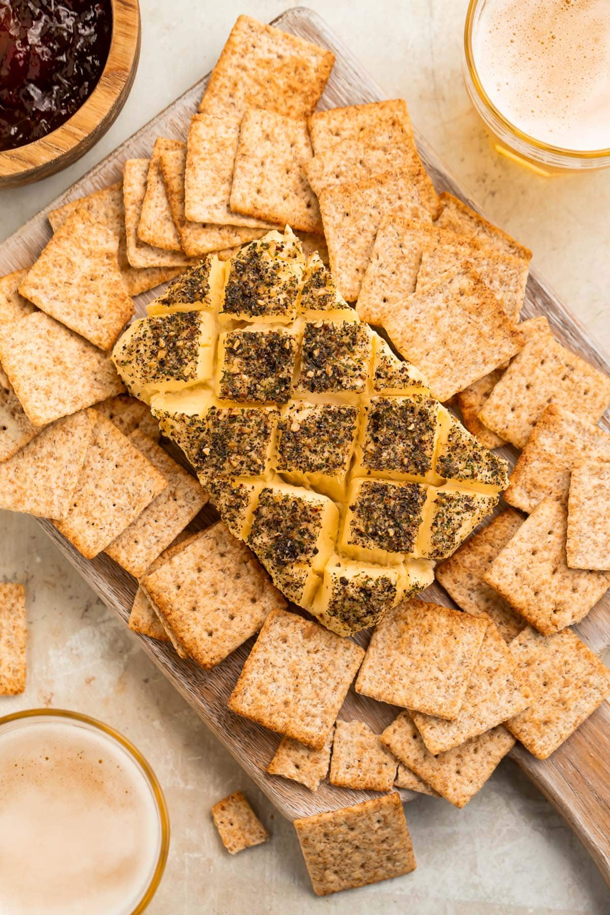 A block of smoked cream cheese, seasoned and crosshatched, surrounded by square wheat crackers.