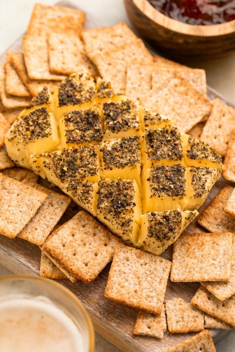 A block of smoked cream cheese, seasoned and crosshatched, surrounded by square wheat crackers.