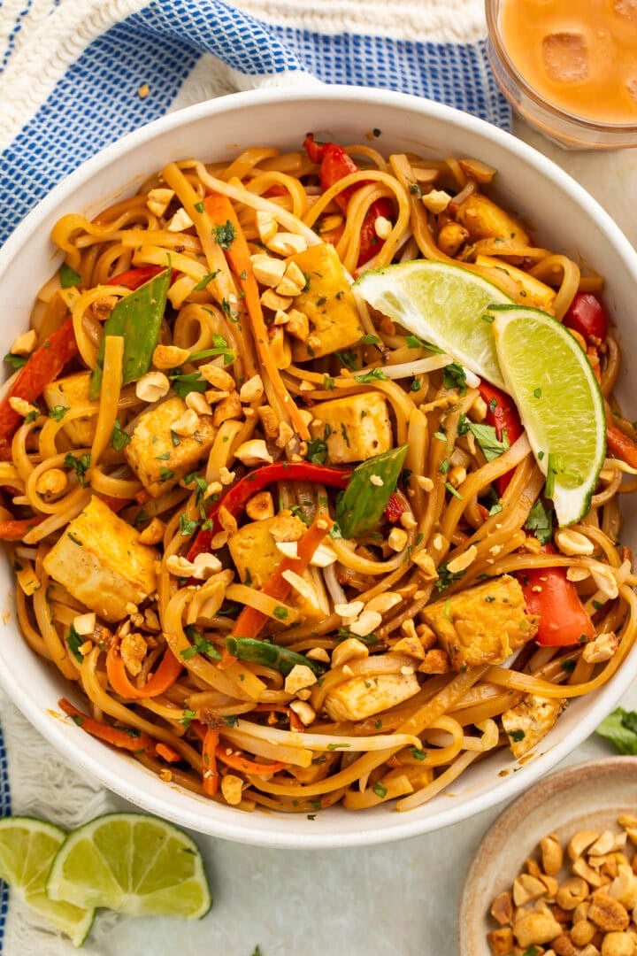 A bowl of vegan pad thai on a table with a blue kitchen towel.