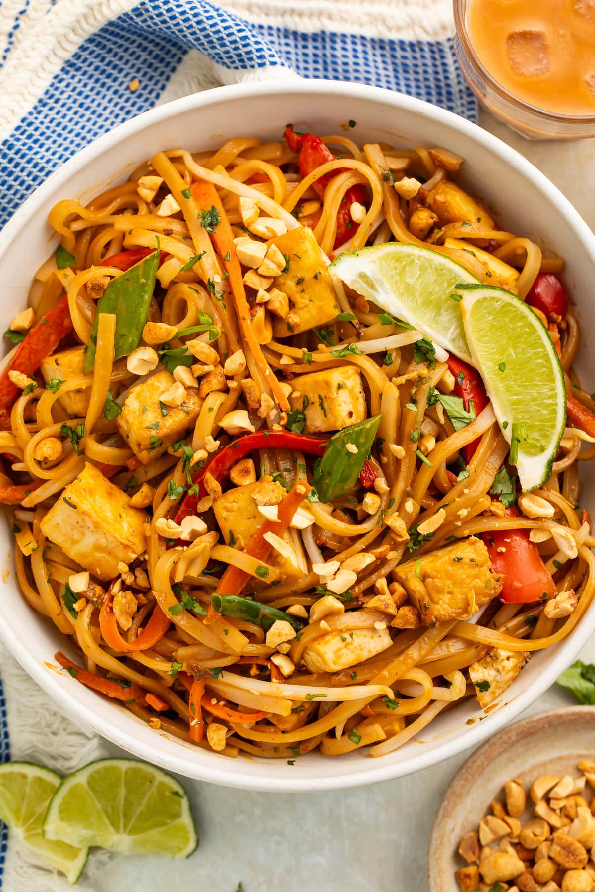 A bowl of vegan pad thai on a table with a blue kitchen towel.