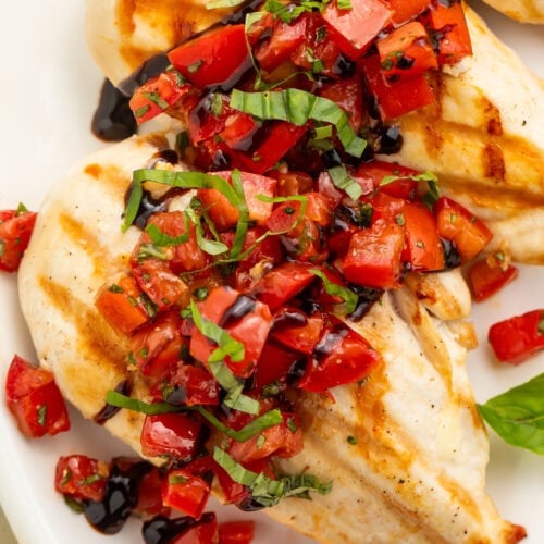 Close up of chicken breasts with bruschetta topping spooned over the top on a white plate.