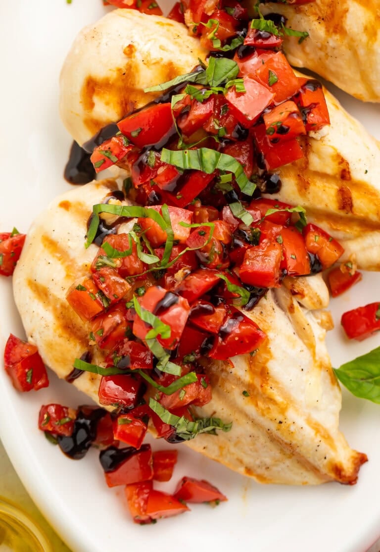 Close up of chicken breasts with bruschetta topping spooned over the top on a white plate.