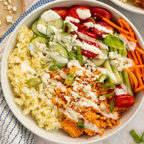 buffalo chicken bowls with shredded chicken, rice, fresh vegetables, and blue cheese crumbles in white bowls