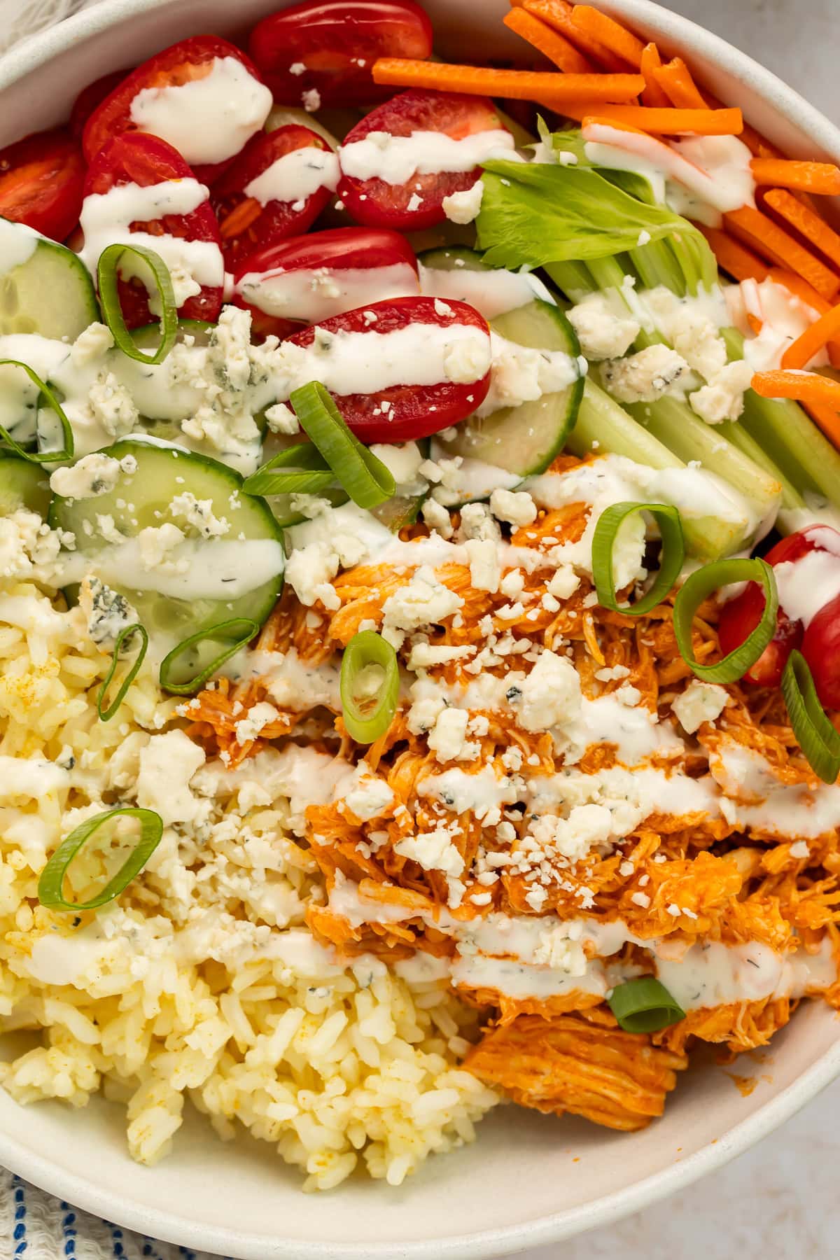 buffalo chicken bowls with shredded chicken, rice, fresh vegetables, and blue cheese crumbles in white bowls