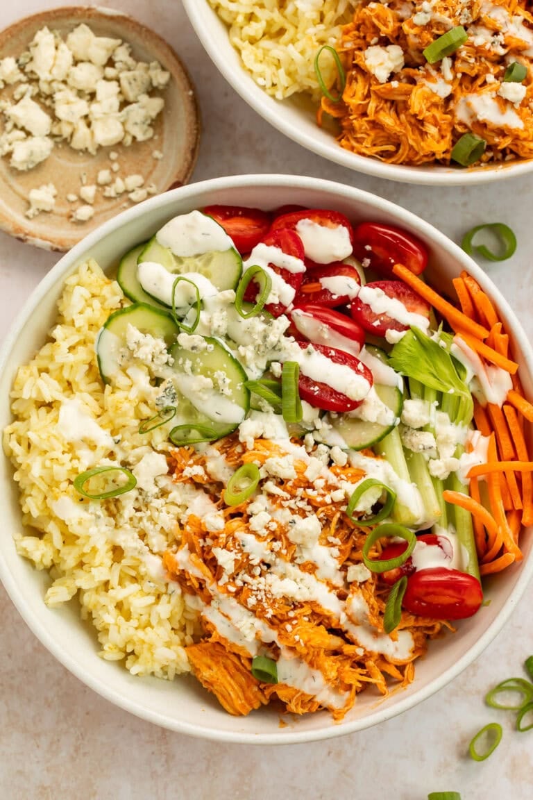 buffalo chicken bowls with shredded chicken, rice, fresh vegetables, and blue cheese crumbles in white bowls