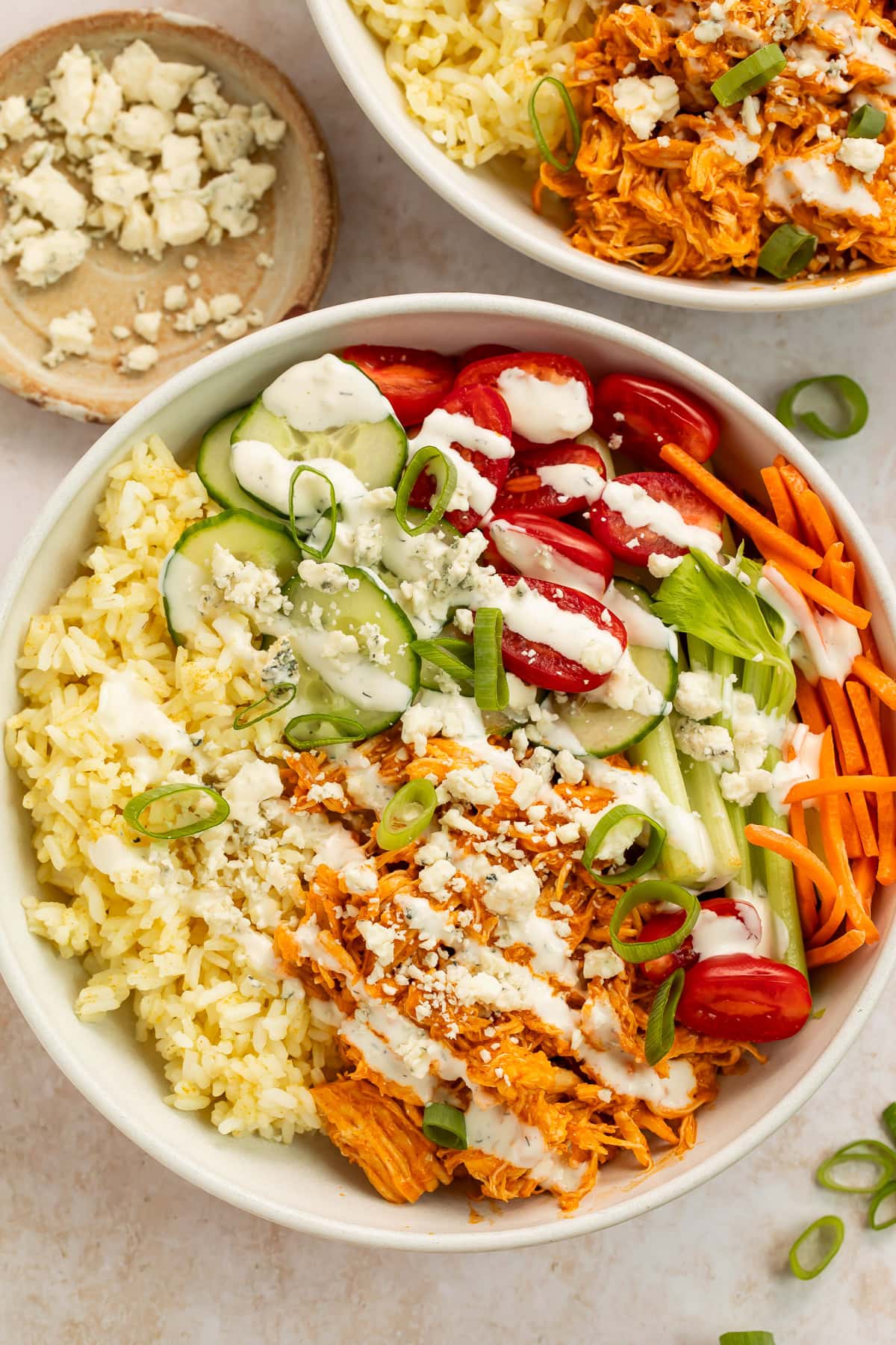 buffalo chicken bowls with shredded chicken, rice, fresh vegetables, and blue cheese crumbles in white bowls