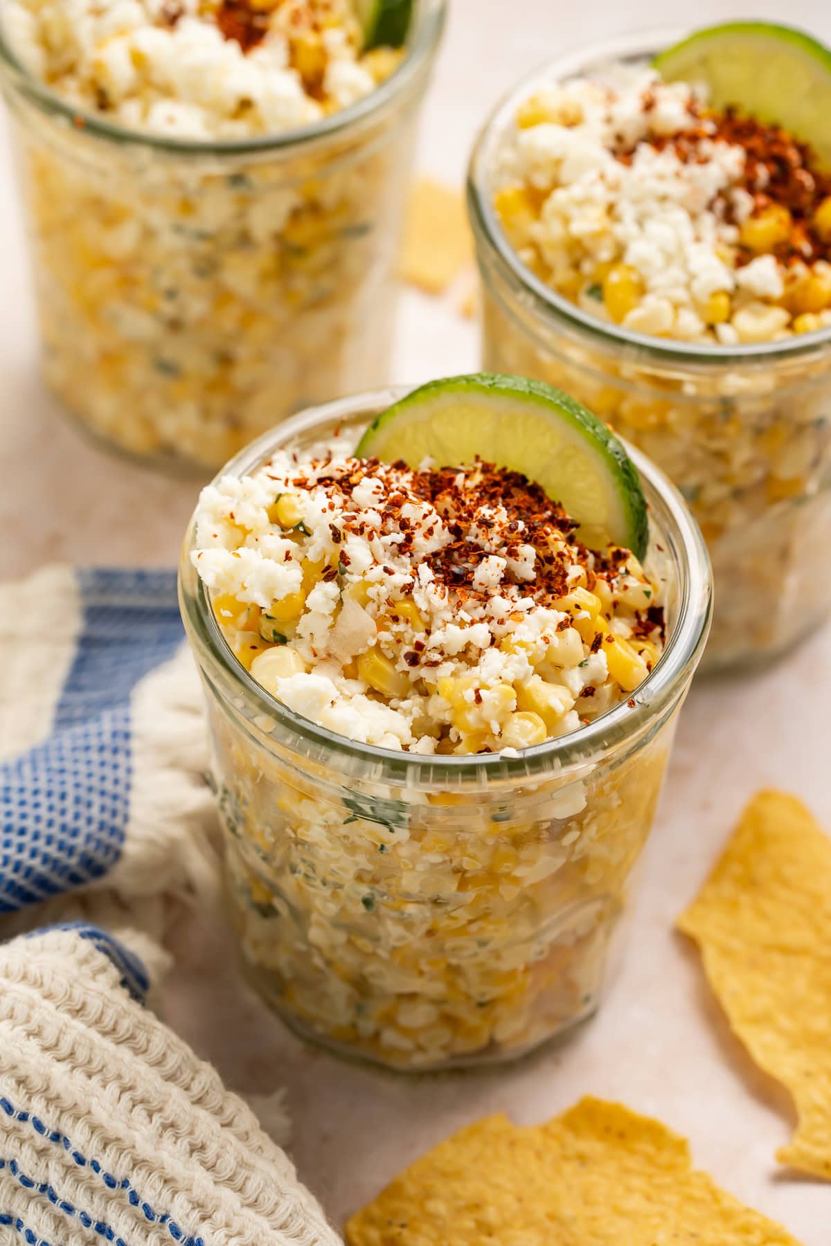 Close up view of esquites in a mason jar with cotija cheese and chili powder on top