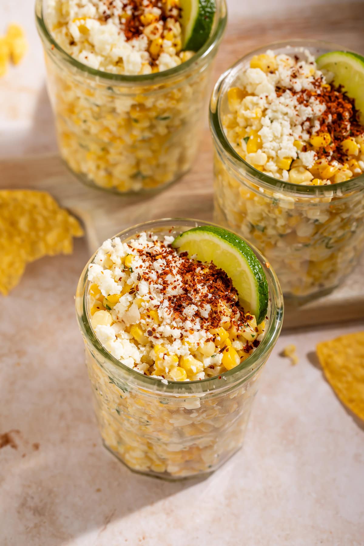 Close up view of esquites in a mason jar with cotija cheese and chili powder on top