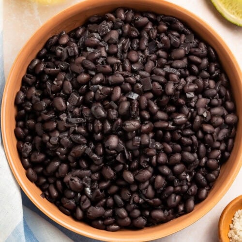 Cooked black beans in terra cotta bowl with lime wedges and olive oil