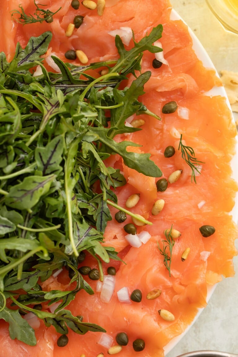 Elegant salmon carpaccio with arugula, capers, and pine nuts on white plate