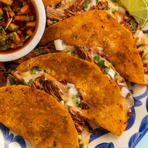 Crispy quesabirria tacos with perfectly melted cheese and tender shredded birria beef, served with rich consommé for dipping. The golden-brown tortillas are beautifully charred and stuffed with savory meat and cheese.