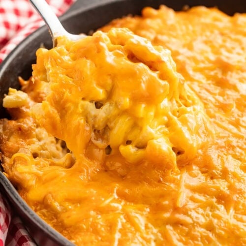 Creamy smoked mac and cheese in a cast iron skillet with a spoon lifting a portion showing the melted cheese texture
