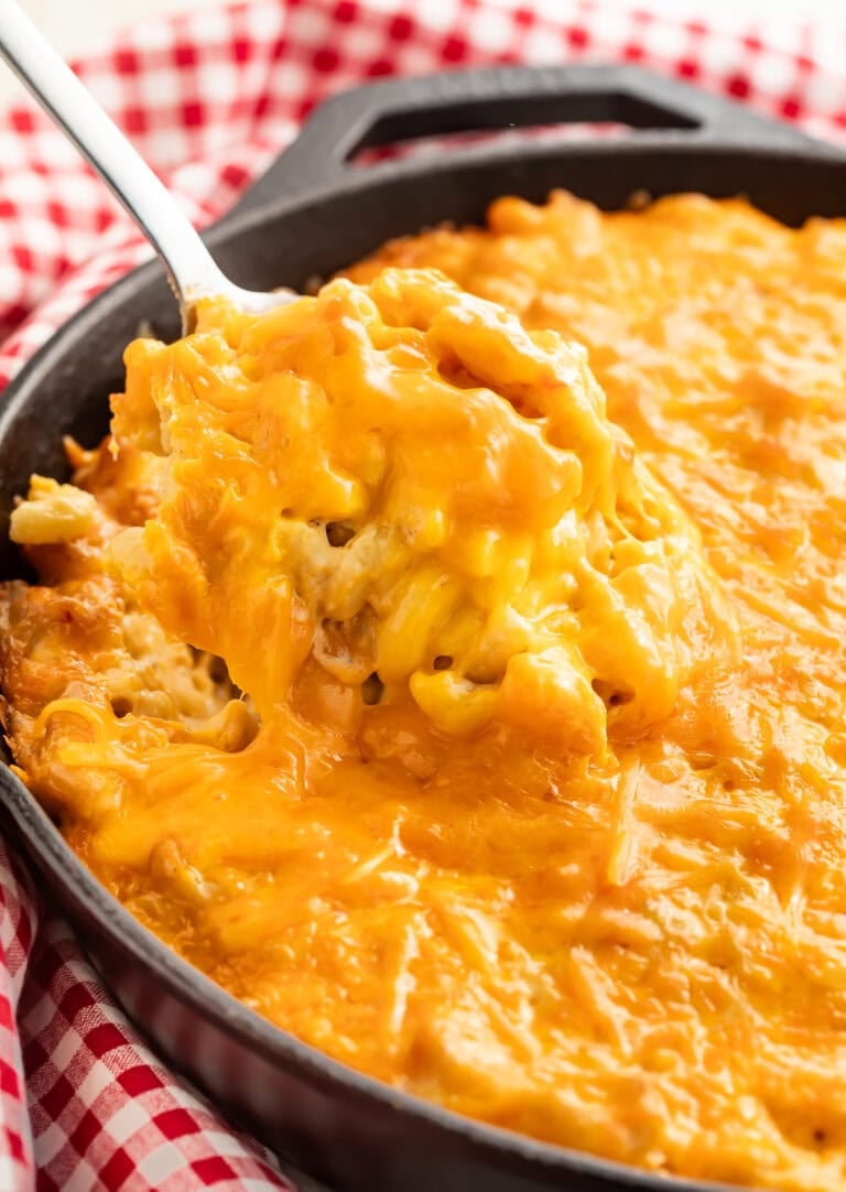 Creamy smoked mac and cheese in a cast iron skillet with a spoon lifting a portion showing the melted cheese texture