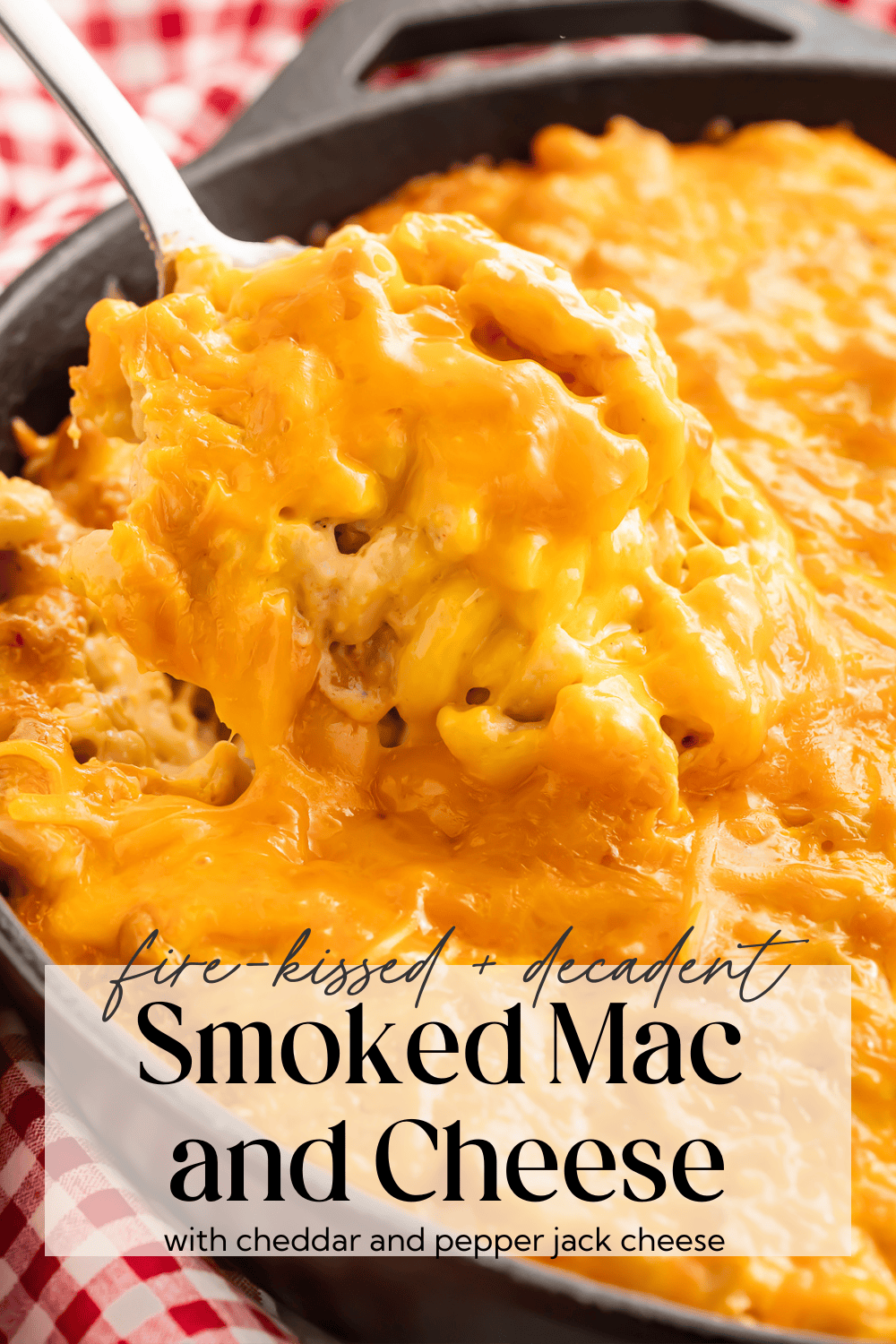 Creamy smoked mac and cheese in a cast iron skillet with a spoon lifting a portion showing the melted cheese texture