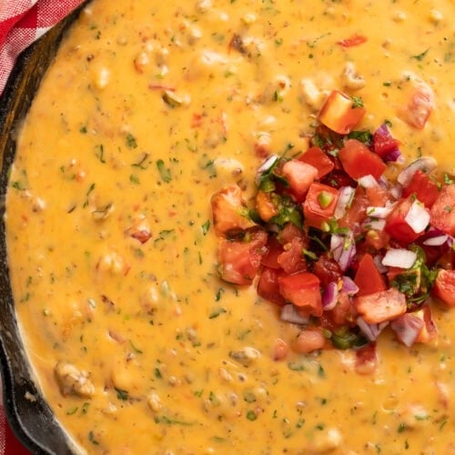 Creamy smoked queso dip with melted cheese and sausage in a cast iron skillet, garnished with fresh cilantro
