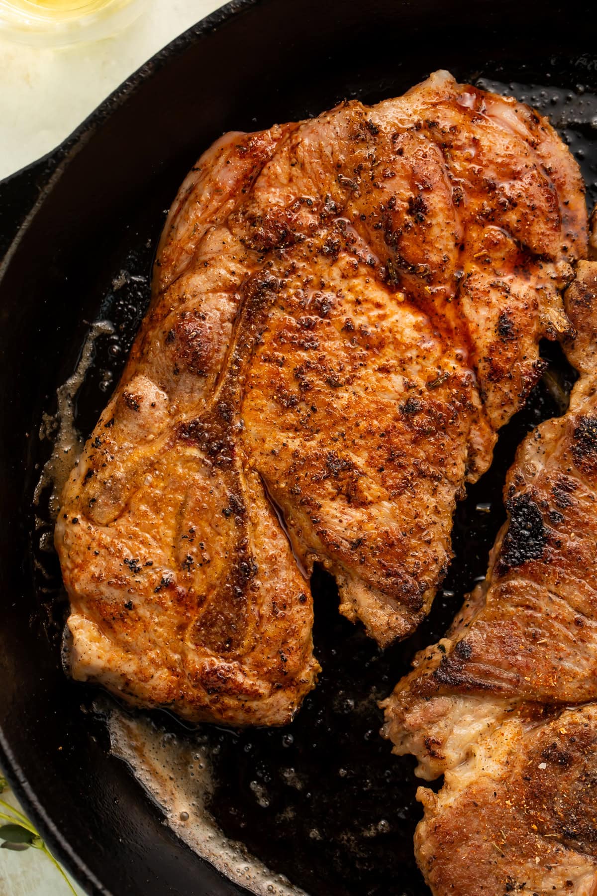 Close-up view of caramelized pork steaks with crispy seasoned crust in cast iron skillet