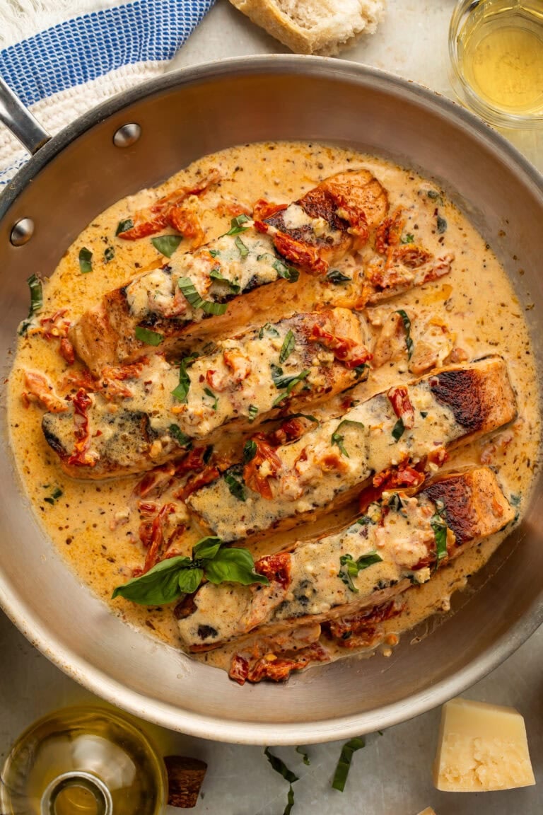Pan-seared salmon with creamy parmesan sauce and sun-dried tomatoes in a stainless steel skillet