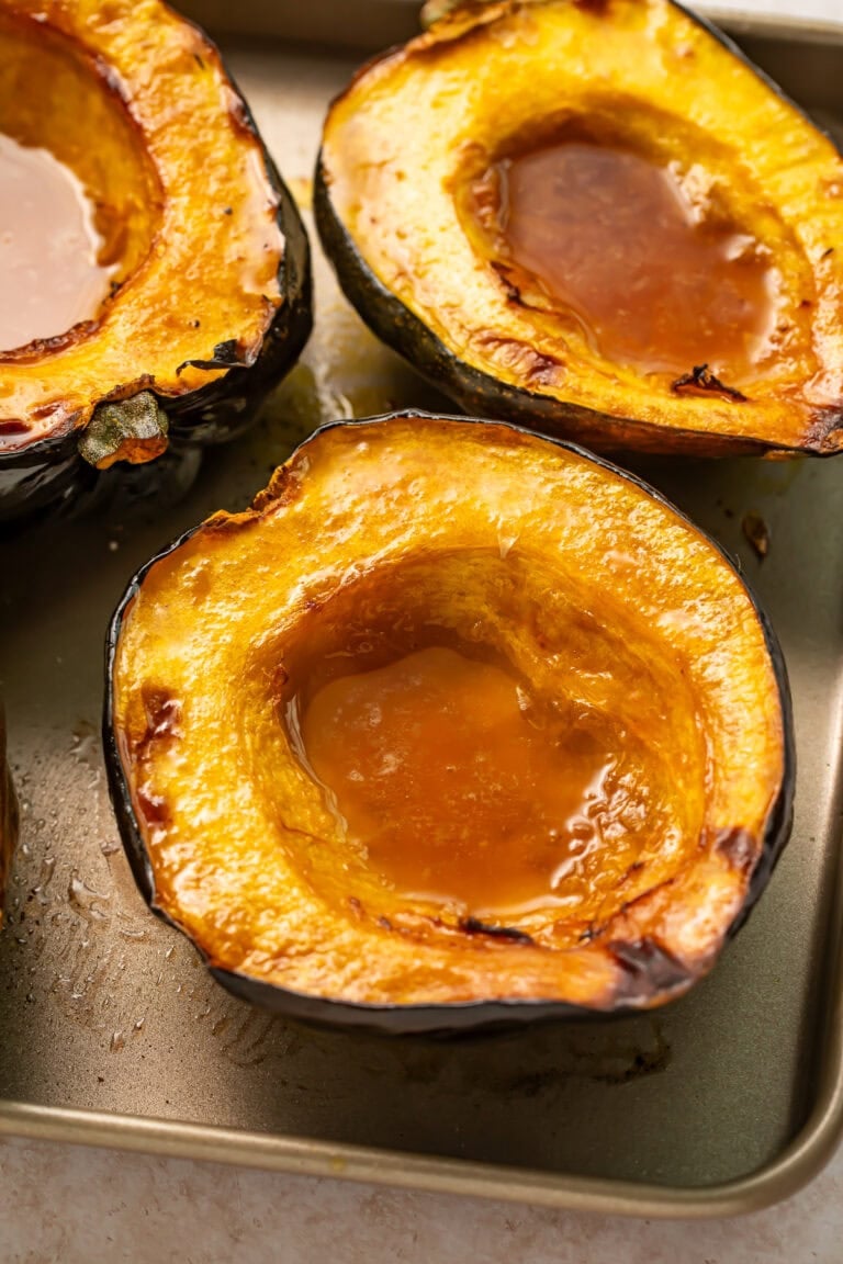 Roasted acorn squash halves with caramelized maple butter pooled in centers on baking sheet