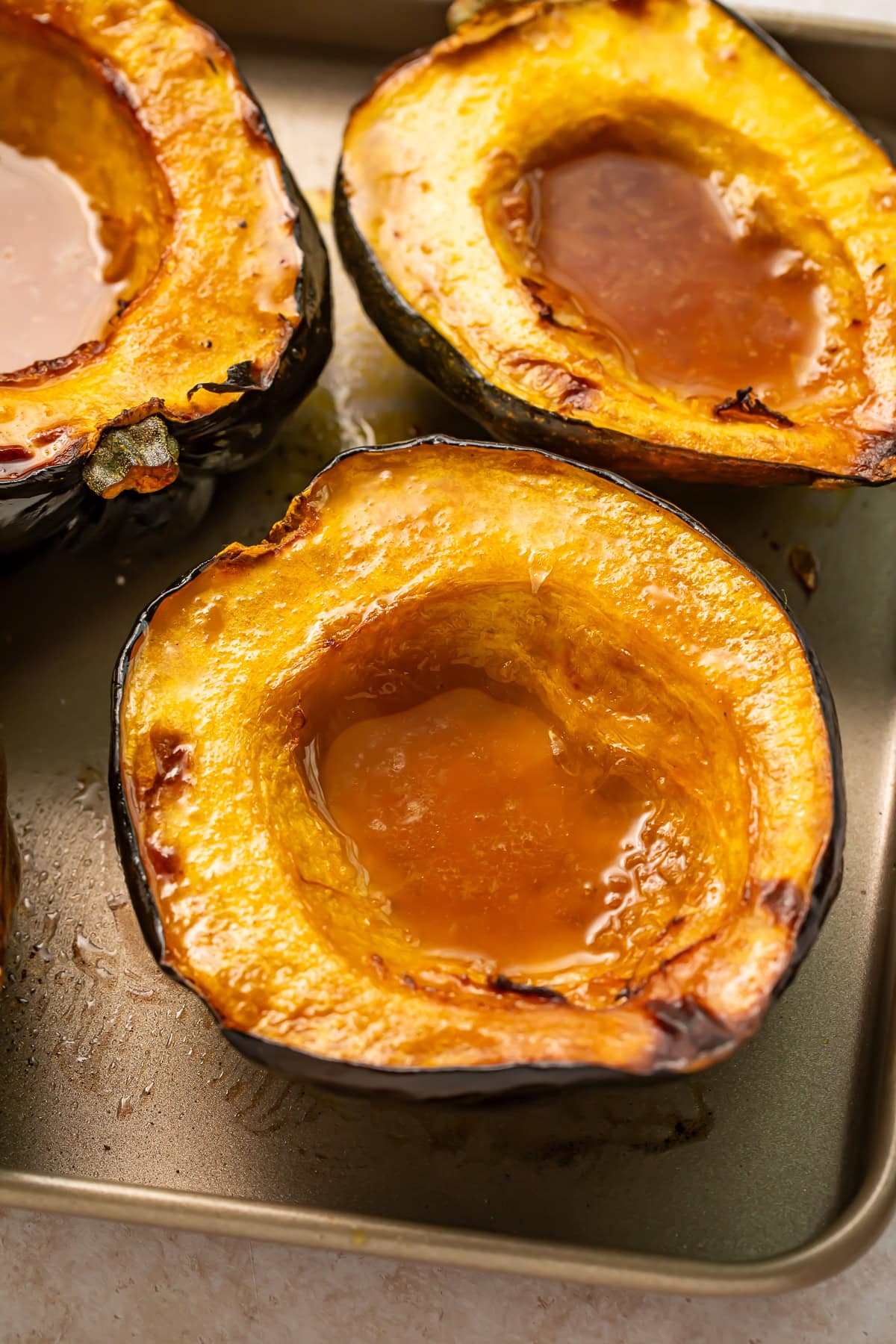 Roasted acorn squash halves with caramelized maple butter pooled in centers on baking sheet