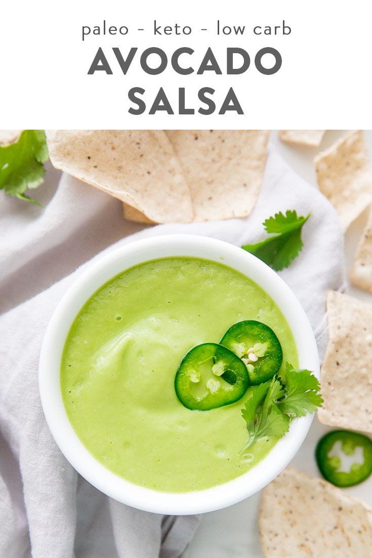 Creamy light green salsa in white ceramic bowl with sliced jalapeños and herb garnish