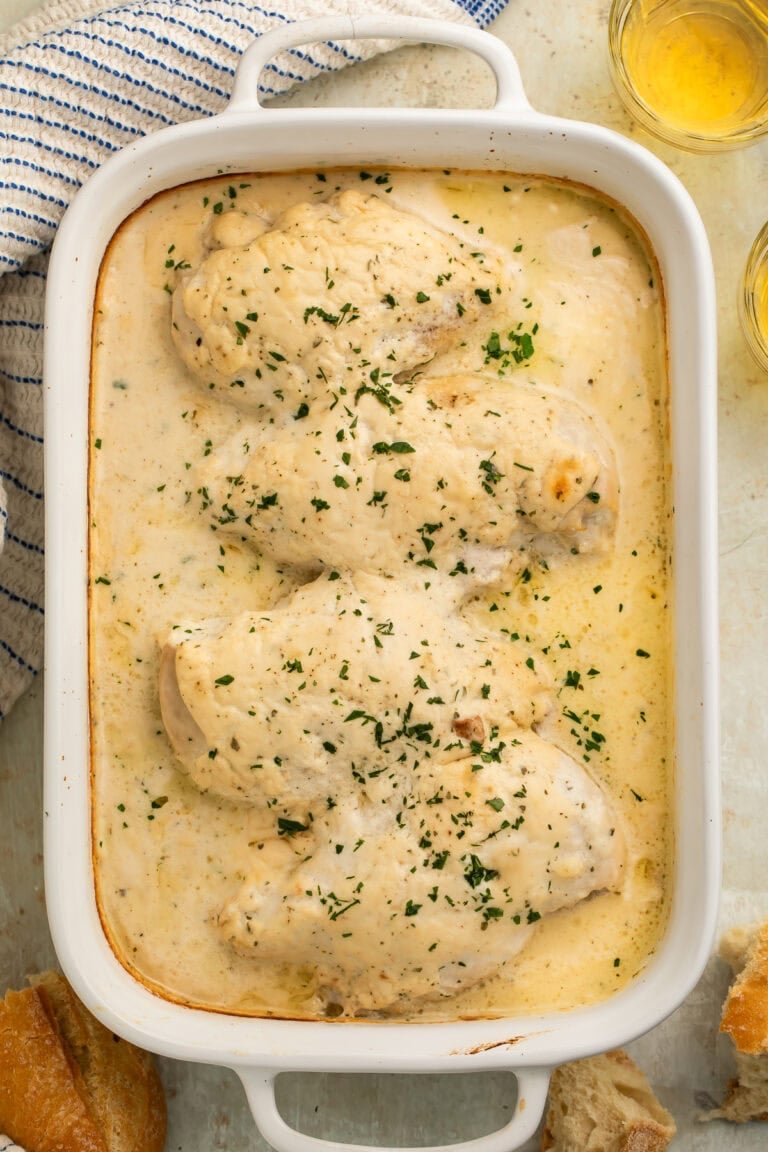 Creamy ranch chicken in white baking dish with golden bubbling sauce and fresh parsley garnish