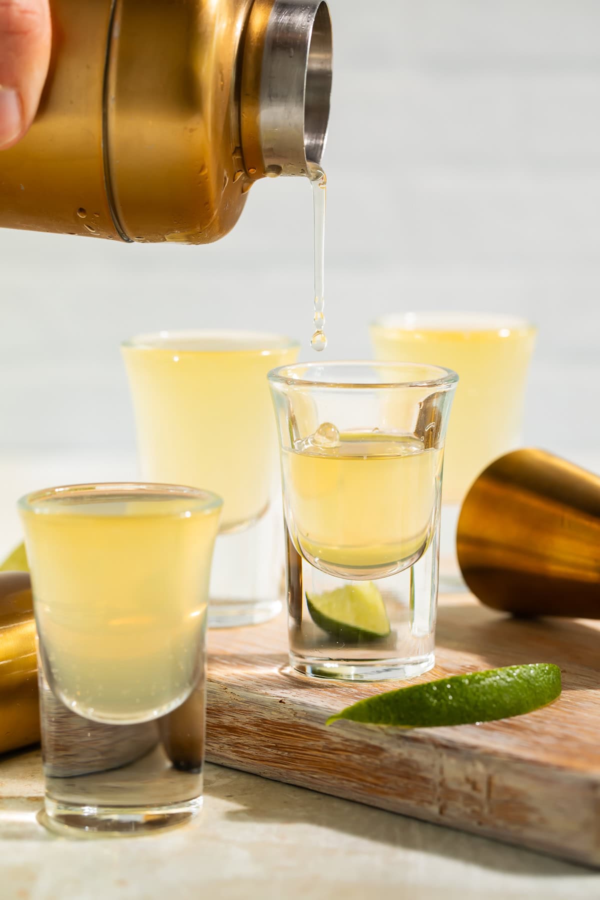 Three green tea shots lined up on bar with lime garnish and cocktail shaker