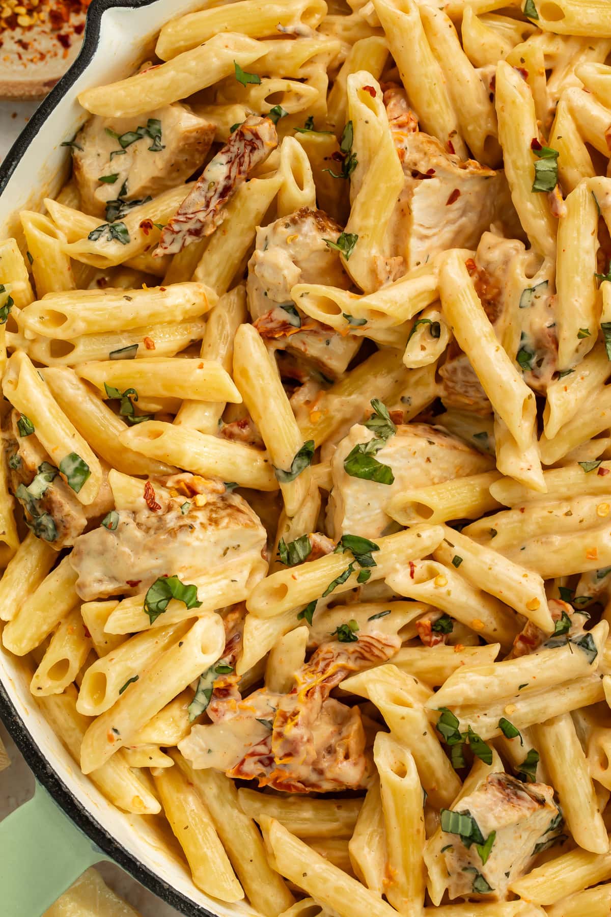 Bowl of marry me chicken pasta garnished with fresh basil and parmesan cheese on dinner table