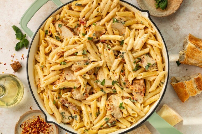 Bowl of marry me chicken pasta garnished with fresh basil and parmesan cheese on dinner table