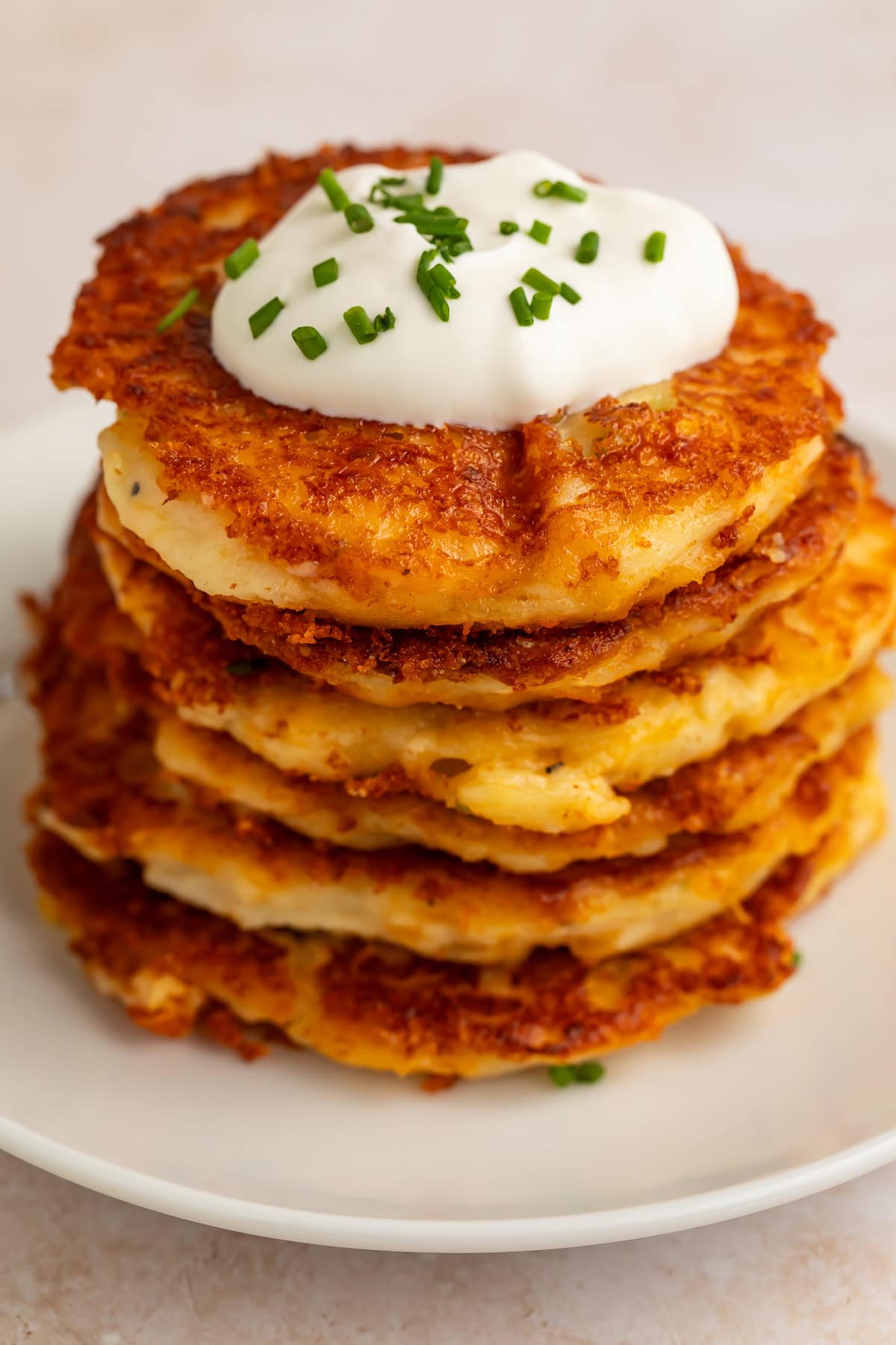 Stack of golden crispy mashed potato pancakes topped with sour cream and chives