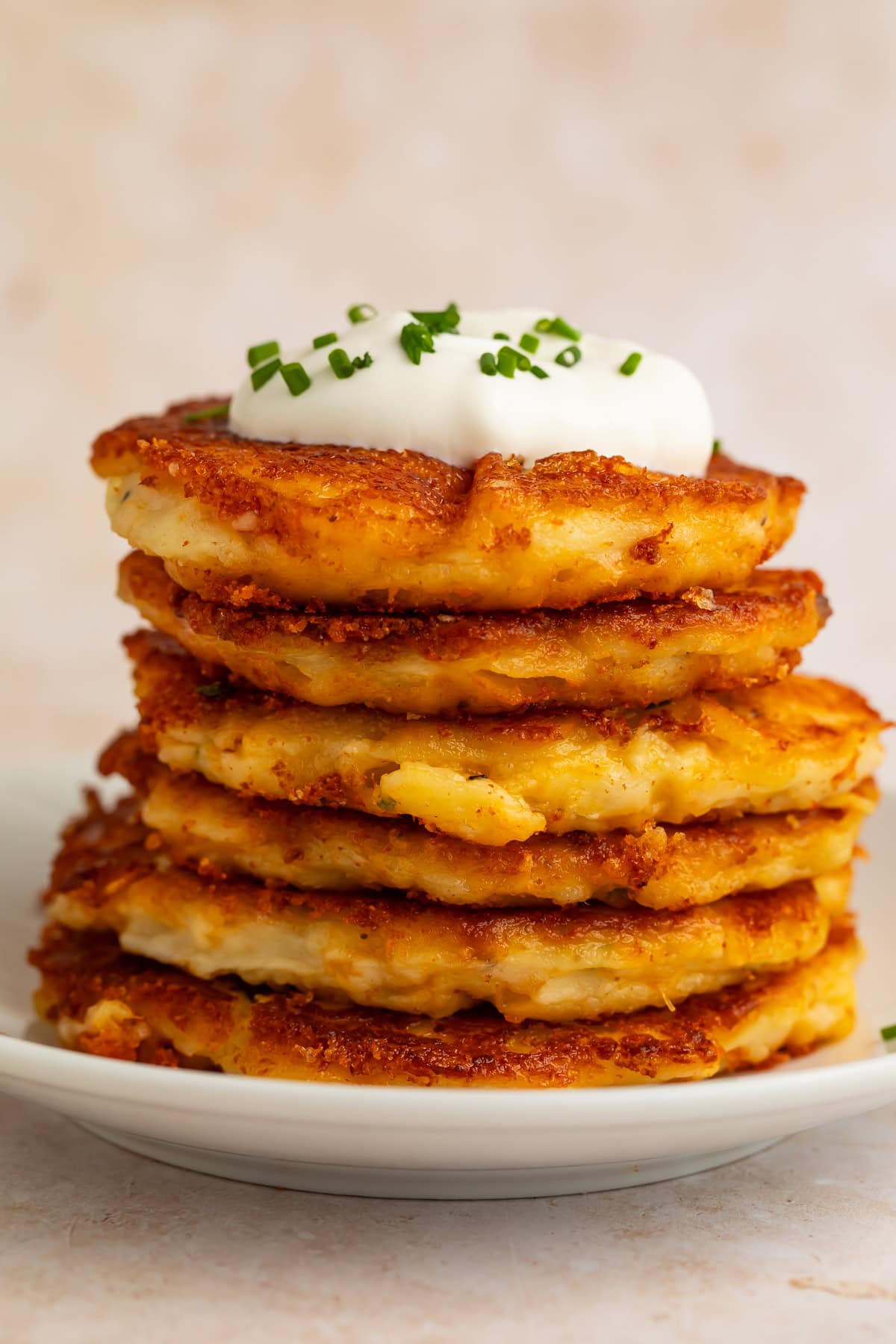 Side view of stacked mashed potato pancakes with sour cream and chives on white plate