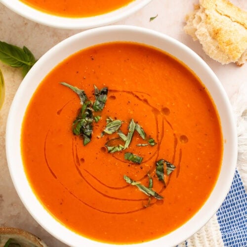 Whole30 tomato soup in white bowls with fresh basil garnish and crusty bread on marble surface