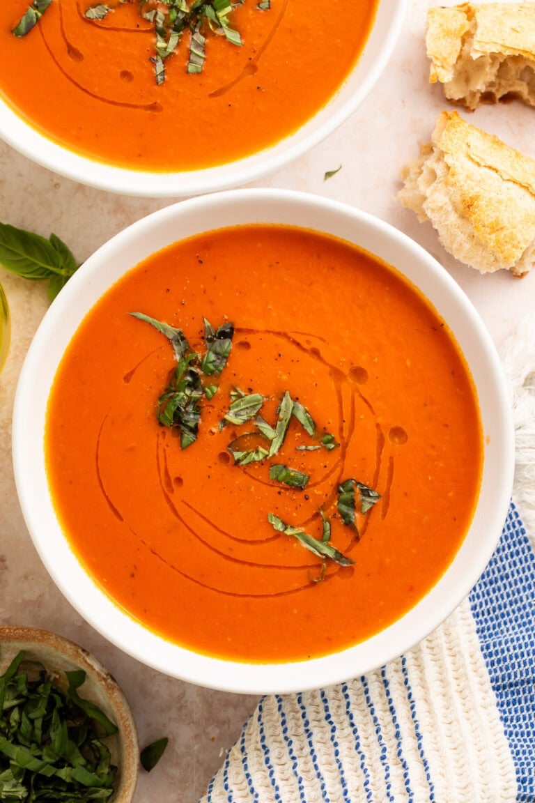 Whole30 tomato soup in white bowls with fresh basil garnish and crusty bread on marble surface