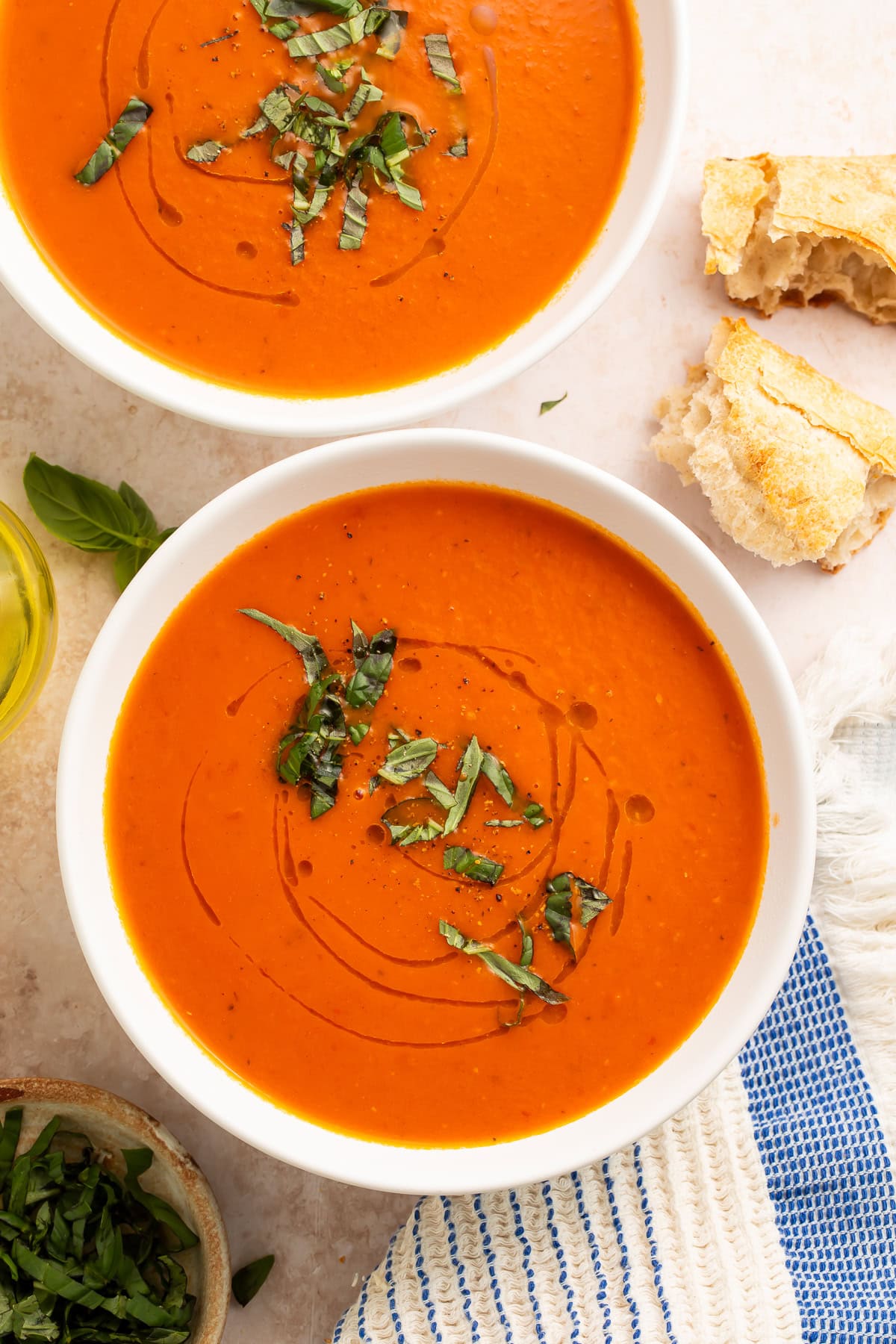 Whole30 tomato soup in white bowls with fresh basil garnish and crusty bread on marble surface