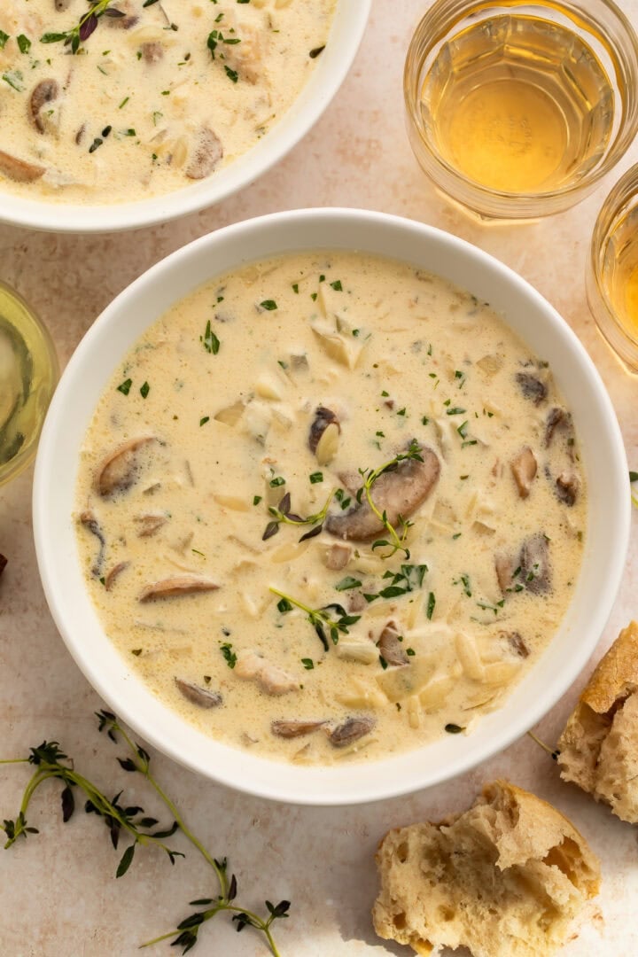 Creamy Boursin chicken mushroom soup served in white bowls garnished with fresh thyme and parsley, alongside white wine and crusty bread
