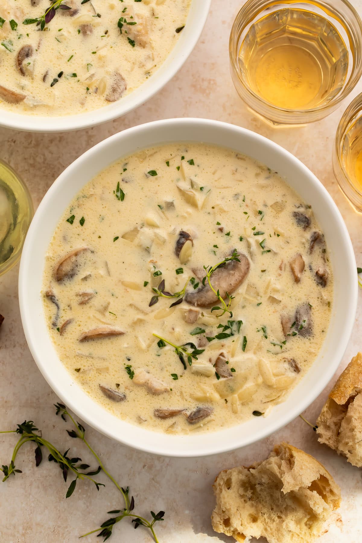 Creamy Boursin chicken mushroom soup served in white bowls garnished with fresh thyme and parsley, alongside white wine and crusty bread