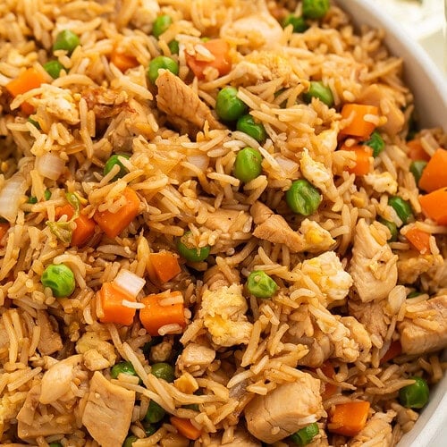 Overhead view of garlic butter chicken fried rice in a white bowl with chicken pieces, peas, and carrots