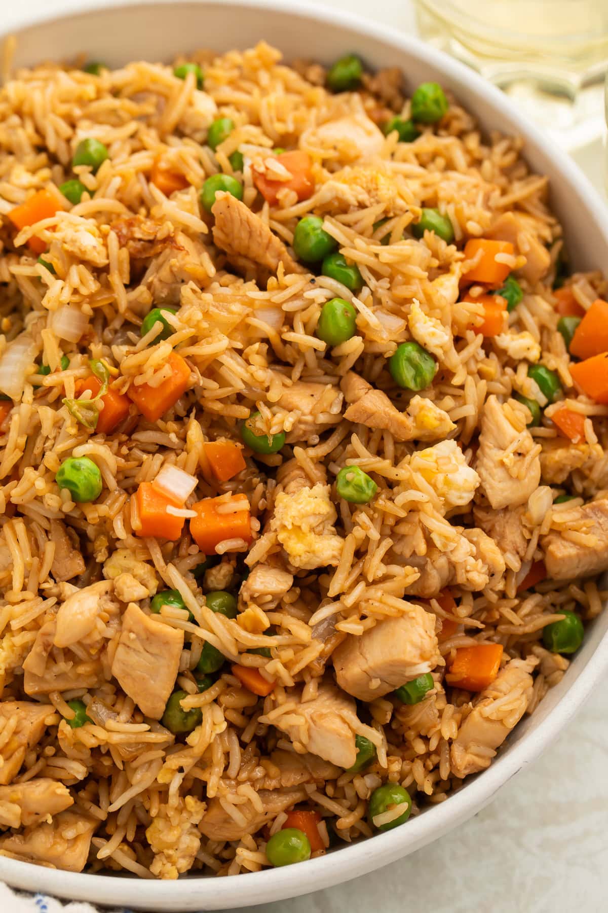 Overhead view of garlic butter chicken fried rice in a white bowl with chicken pieces, peas, and carrots