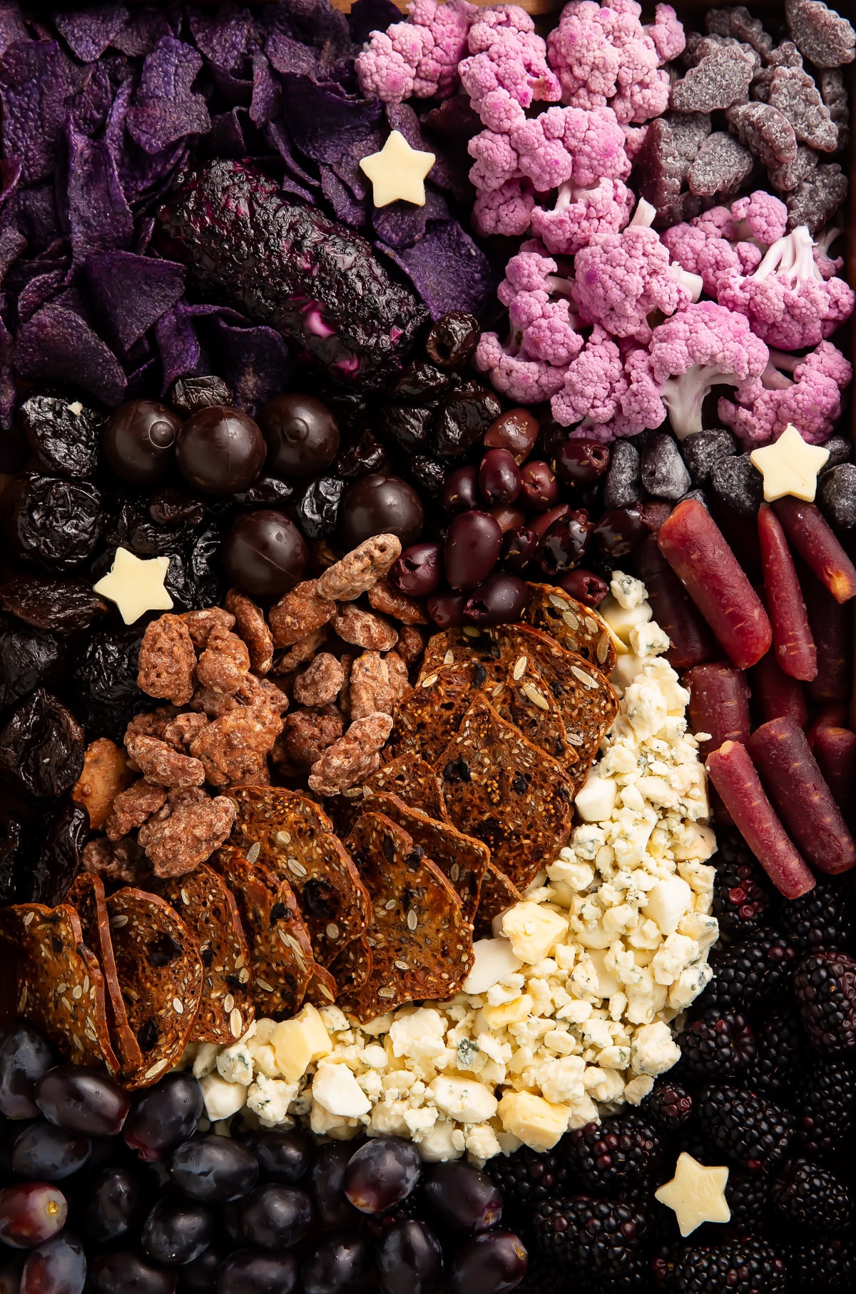 Halloween moon charcuterie board with purple cauliflower, black grapes, white cheese, and star decorations arranged on dark background